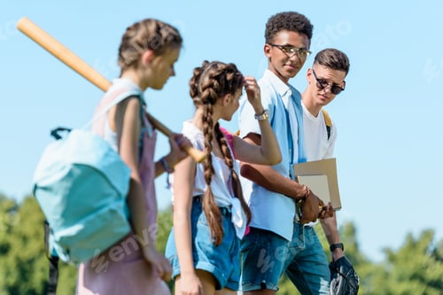 Preview: side view of multiethnic teenage students with books, backpacks and sport equipment walking together