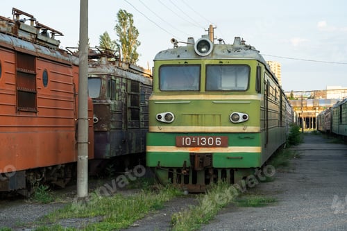 Preview: Decommissioned orange and green soviet locomotives stand on overgrown railway in abandoned stock