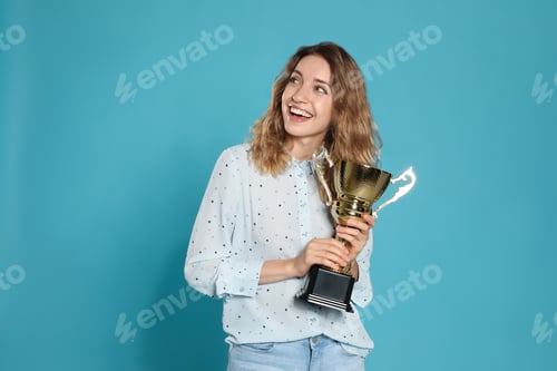 Preview: Portrait of happy young woman with gold trophy cup on blue background