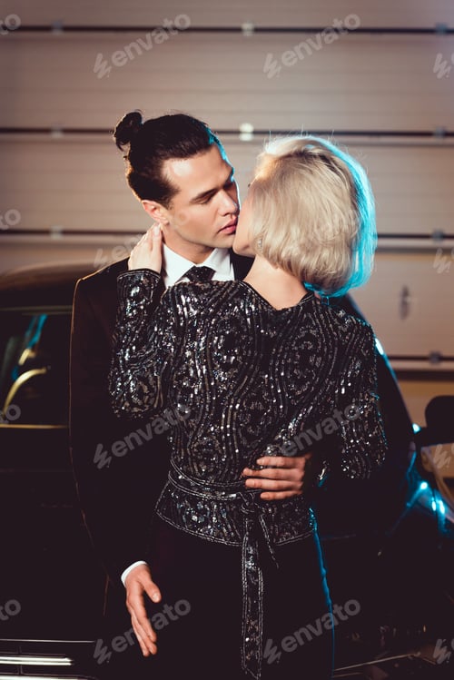 Preview: stylish couple in formal wear kissing near car