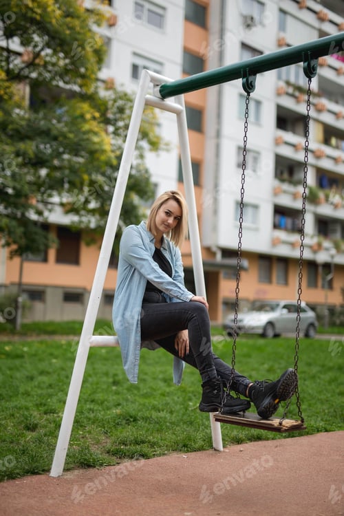 Preview: Vertical shot of a beautiful Caucasian female posing on a swing in a park