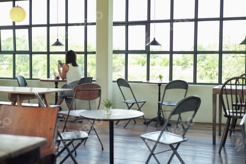 Preview: Rear view of woman sits in the coffee shop with empty wooden furniture