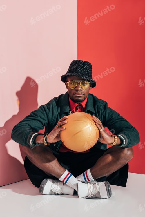 Preview: fashionable african american man in sunglasses holding golden basketball ball and looking at camera