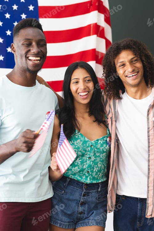 Preview: Young African American man, biracial woman, and biracial man smile with American flags in hand