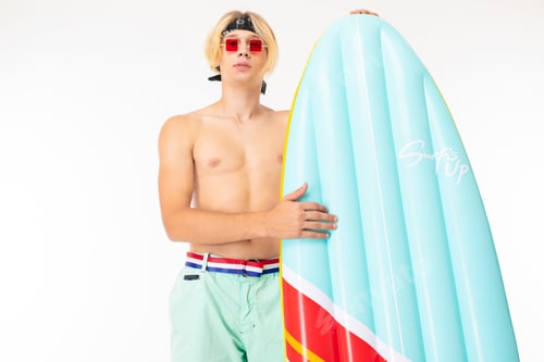 Preview: stylish blond man with an air mattress in the form of a surfboard on a white background