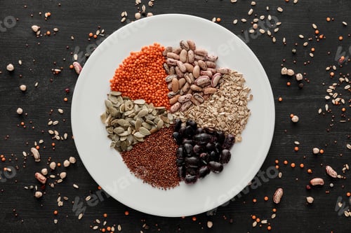 Preview: top view of white ceramic plate with raw assorted beans, cereals and seeds on dark wooden surface