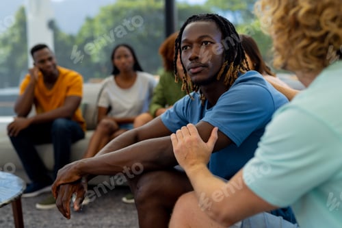 Preview: Group of diverse people sitting on sofa and talking in group therapy session