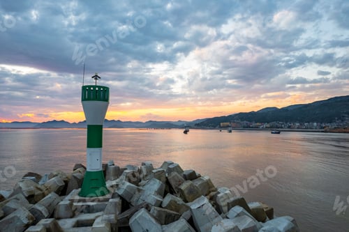 Preview: Lighthouse on the stony long pier near the coastal town at sunset