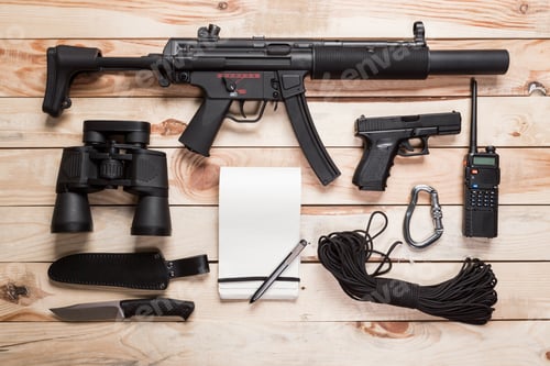 Preview: Assault rifle, gun, knife with sheath, compass and notebook with pen on table.