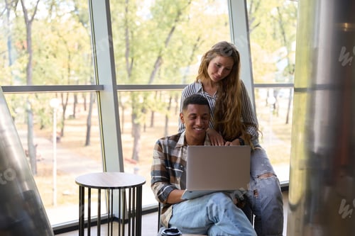 Preview: Couple in love looking at laptop screen against large window