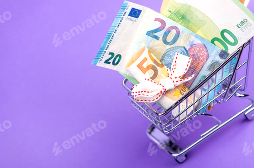 Preview: roll of euro banknotes with white ribbon in supermarket trolley cart isolated on purple background