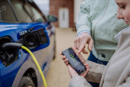 Preview: Close up of man and his daughter holding smartphone, checking charging of his electric car.