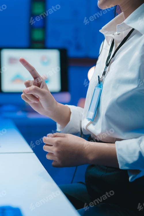 Preview: Businesswoman pointing at computer screen with charts displayed in modern office at night