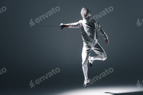Preview: Professional fencer in fencing mask with rapier jumping isolated on grey