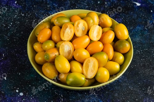 Preview: Close up photo of kumquats in ceramic bowl over blue background