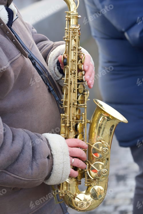 Preview: Unrecognizable street musician plays saxophone outside on the street in the cold wintertime