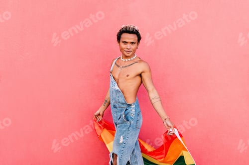 Preview: Young man walking with rainbow flag against pink wall