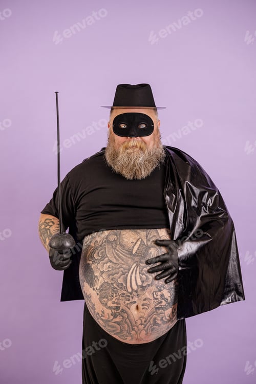 Preview: Gentleman with overweight in Zorro costume shows large bare tummy with tattoos on purple background