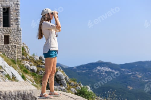 Preview: Young woman watching mountain landscape through binoculars at the view spot on tourist trail