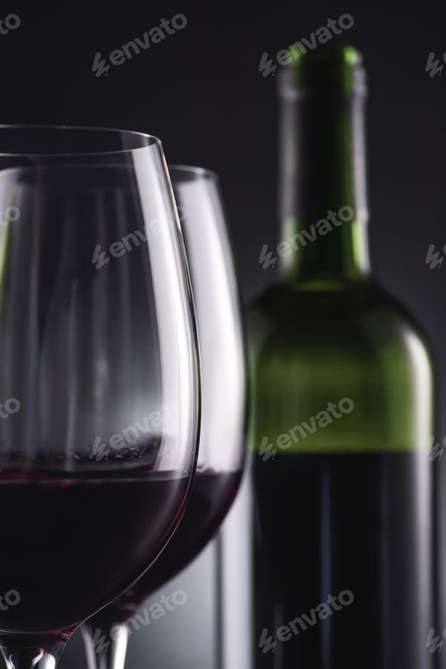 Preview: close-up shot of glasses filled with red wine and wine bottle blurred on background