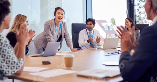 Preview: Multi-Cultural Business Team Applauding Businesswoman Leading Meeting Around Table In Modern Office