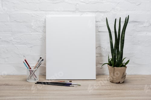 Preview: close up view of empty drawing easel, paintbrushes and plant in flowerpot on table