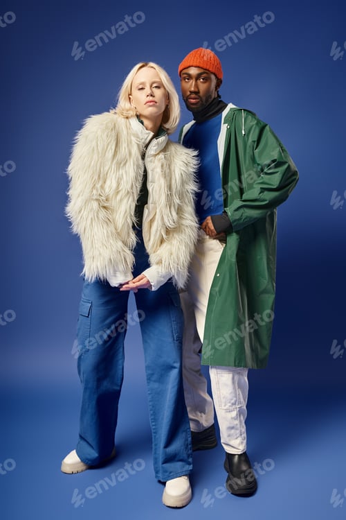 Preview: stylish interracial models in winter attire on blue backdrop, blonde woman and african american man