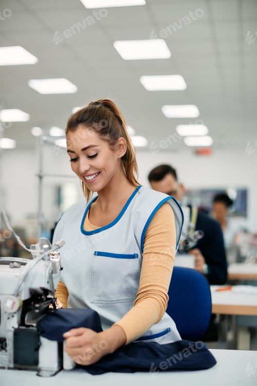 Preview: Young happy textile worker sewing at production line in clothing factory.