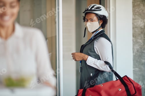 Preview: African American courier with face mask leaving after delivering food at business office.