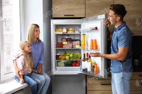 Preview: Happy family near refrigerator full of products in kitchen
