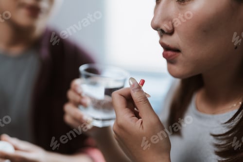 Preview: Young woman taking medicine with glass of water assisted by her doctor