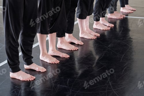 Preview: Row of legs of barefoot young dancers in black pants standing on the floor