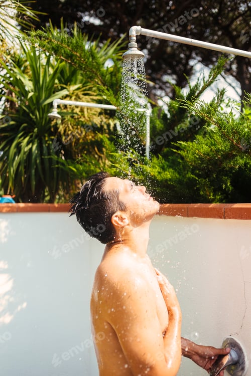 Preview: Young man cooling off with a refreshing outdoor shower on a sunny day
