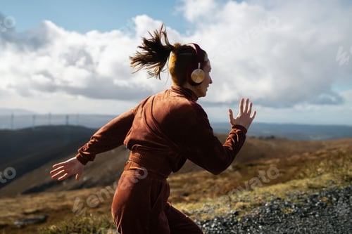 Preview: Young sportswoman running in nature listening to music with headphones