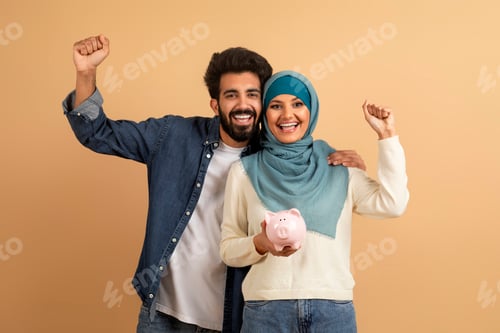 Preview: Happy Young Muslim Couple Holding Piggy Bank And Celebrating Success