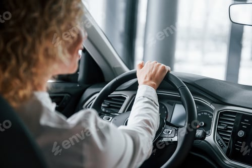 Preview: Rear view. Woman with curly blonde hair is in autosalon