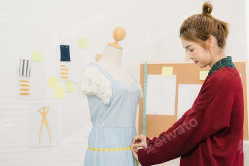 Preview: Asian female fashion designer working measuring dress on a mannequin clothing design at the studio.