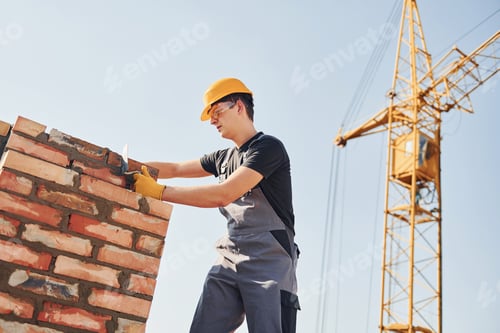 Preview: Installing brick wall. Construction worker in uniform and safety equipment have job on building