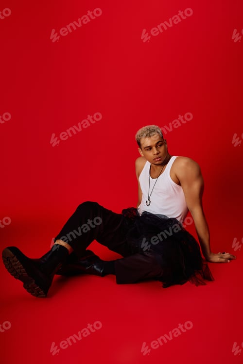 Preview: Stylish young african american man with dyed hair poses in vibrant red studio setting