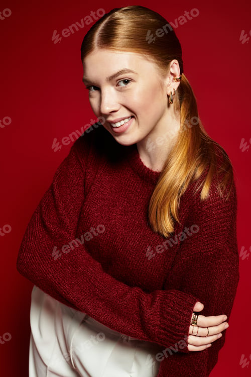 Preview: Young woman showcases cozy winter fashion in vibrant red setting