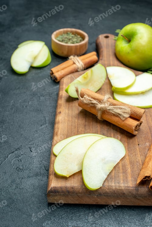 Preview: top view apple slices and cinnamon sticks on wood serving board dried mint powder in wooden bowl on