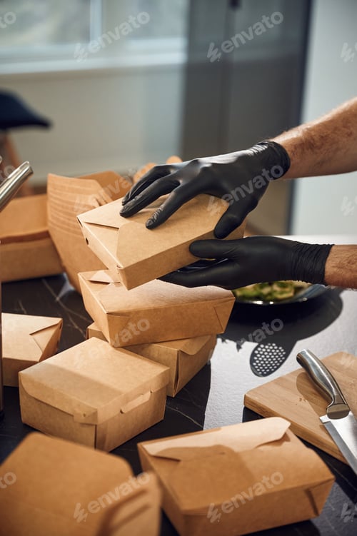 Preview: Man is packing food into the paper eco boxes. Indoors, restaurant