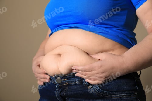 Preview: Overweight woman in tight shirt and jeans on light brown background, closeup
