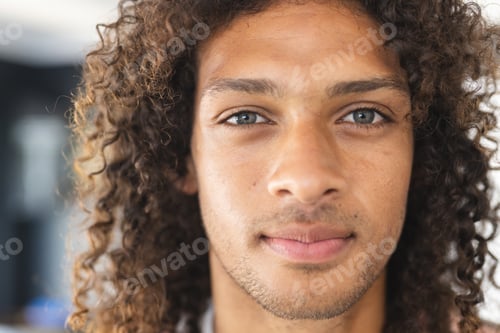 Preview: Young biracial man with curly hair and light brown eyes looks directly at the camera
