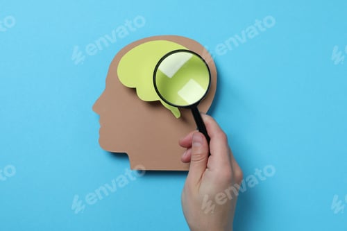 Preview: Magnifying glass in hand and paper head on blue background, top view