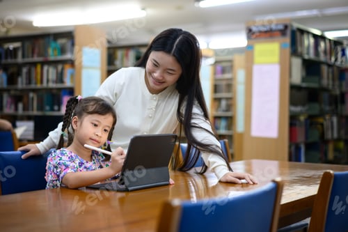 Preview: Asian woman teaching little girl to use digital tablet in library, learning together
