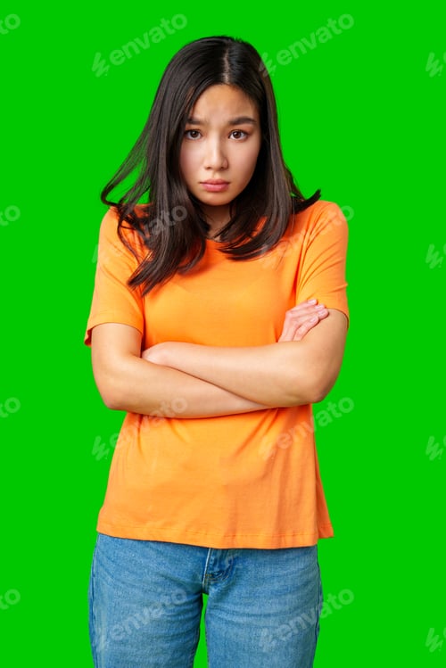 Preview: Young woman with crossed arms showing serious expression against bright green backdrop