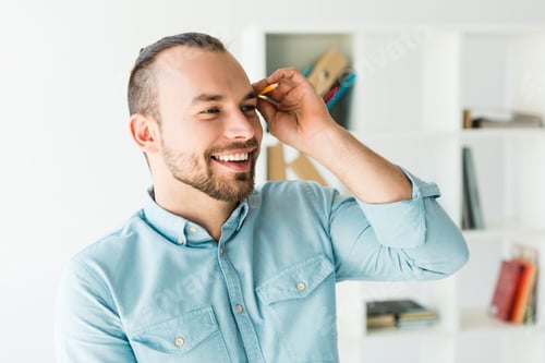 Preview: Portrait of a young smiling man putting pencil behind his ear