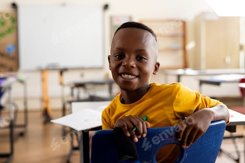 Visualização: Menino afro-americano sentado de costas na cadeira azul na sala de aula, segurando um lápis verde, espaço de cópia