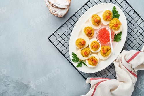 Preview: Stuffed eggs with red caviar and paprika on plate for appetizer easter table, top view, copy space.